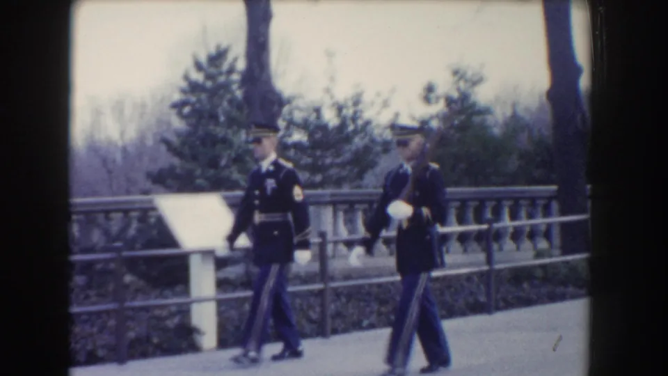 Two guards in ceremonial uniforms march past a sign or marker near a stone balustrade in 1960 Washington, DC footage.