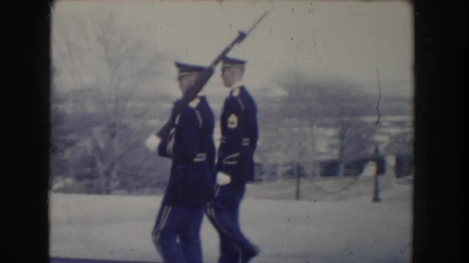 Two soldiers in dark dress uniforms and white gloves march with rifles and fixed bayonets in Washington, DC archival footage.