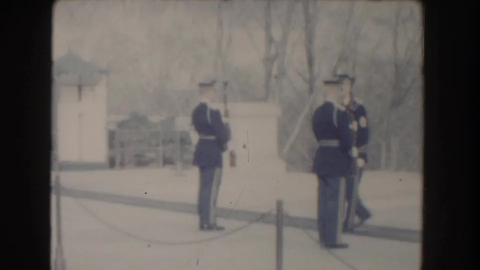 Two uniformed soldiers are seen near pale monument walls, low chain posts, and bare trees in Washington, DC archival home-movie footage.