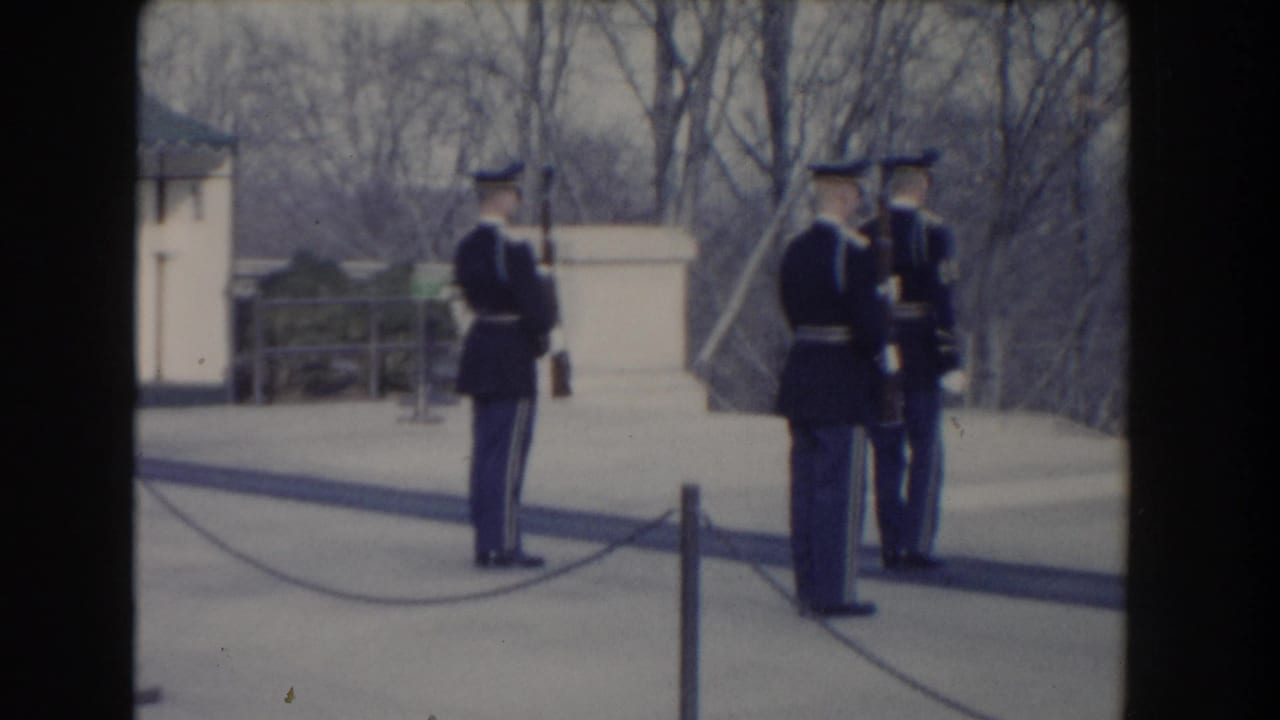 Three uniformed soldiers stand with rifles on a paved outdoor terrace.