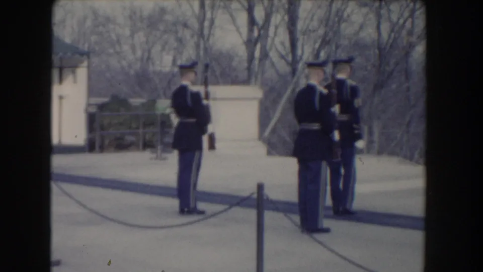 1960 Washington, DC home-movie frame showing three uniformed soldiers with rifles standing on a paved terrace near bare trees.
