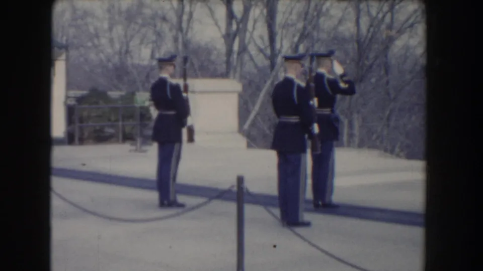 1960 Washington, DC frame showing soldiers in dark uniforms with rifles as one appears to salute during ceremonial drill.