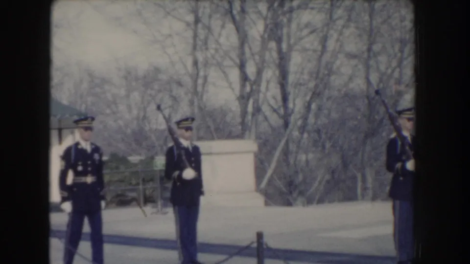Military honor guards in Washington, D.C. stand at attention beside a stone monument, with rifles and white gloves visible.