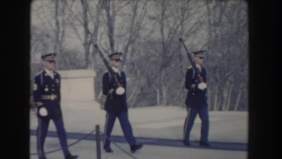 A uniformed guard marches past two standing guards during a formal outdoor ceremony in 1960 Washington, D.C.