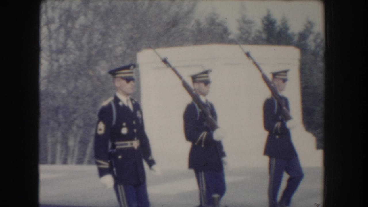 Three soldiers in dress uniforms pass a pale structure while carrying rifles.