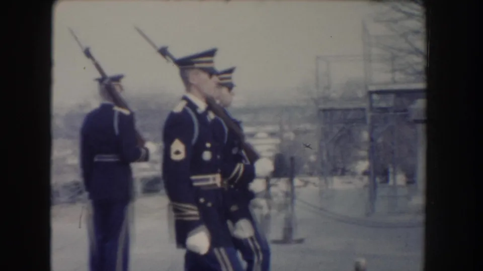 Washington, DC 1960 frame of uniformed soldiers with rifles near ropes, posts, and winter trees in a public ceremonial setting.