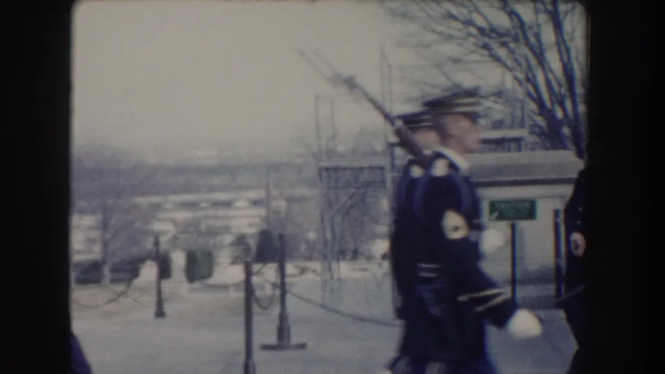 1960 Washington, DC home-movie frame showing U.S. Air Force honor guards marching with rifles near a stone balustrade and winter trees.
