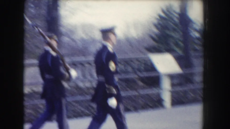 Soft 8mm frame from Washington, DC in 1960 showing honor guards marching near a signboard, stone balustrade, and winter trees.