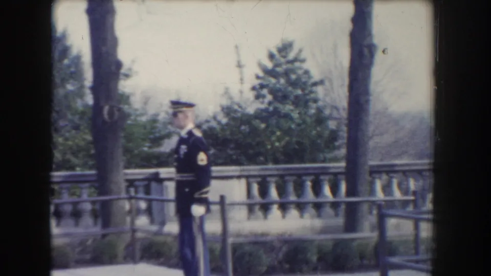 1960 Washington, DC home-movie frame showing the guard at attention near a tree, railing, and formal stone terrace.