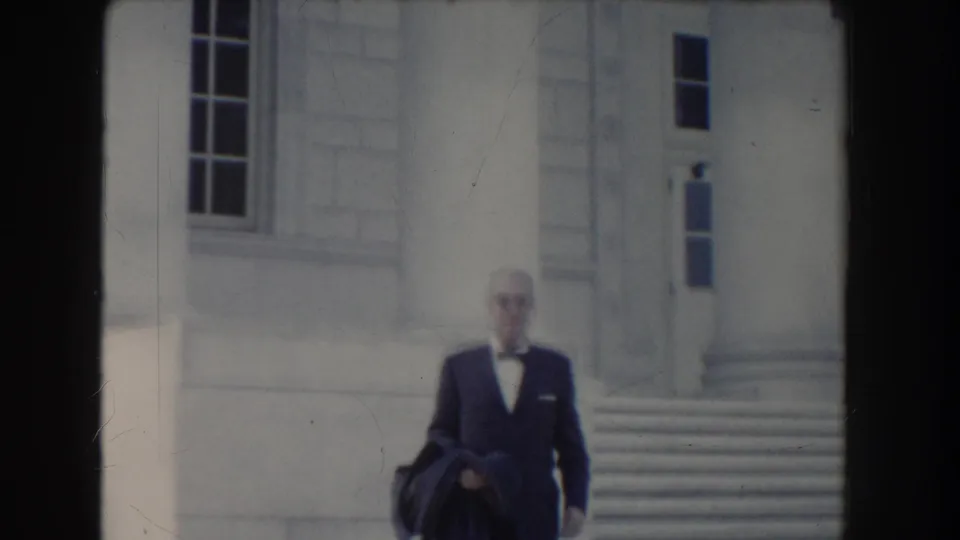 In Washington DC circa 1960, the suited man passes through a soft, slightly blurred frame outside the white public building.