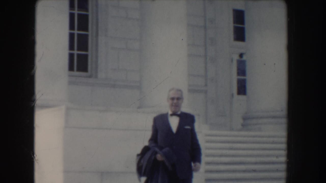 Man in dark suit and bow tie descends stone steps outside a columned building.