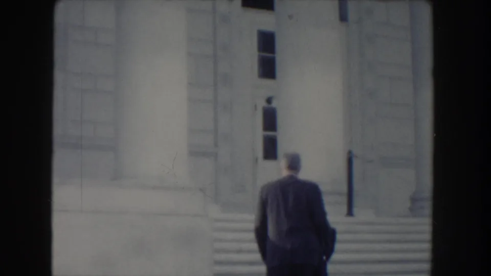 Seen from behind, the formally dressed man approaches the steps of a pale stone classical building in 1960 Washington, DC footage.