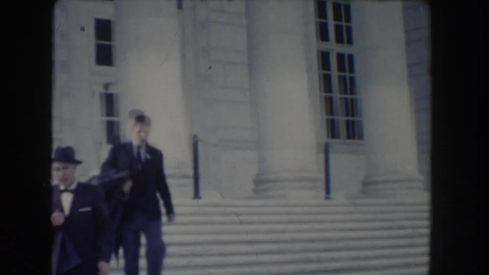 Two formally dressed men walk near broad steps and columns in this 1960 Washington, DC home-movie frame.