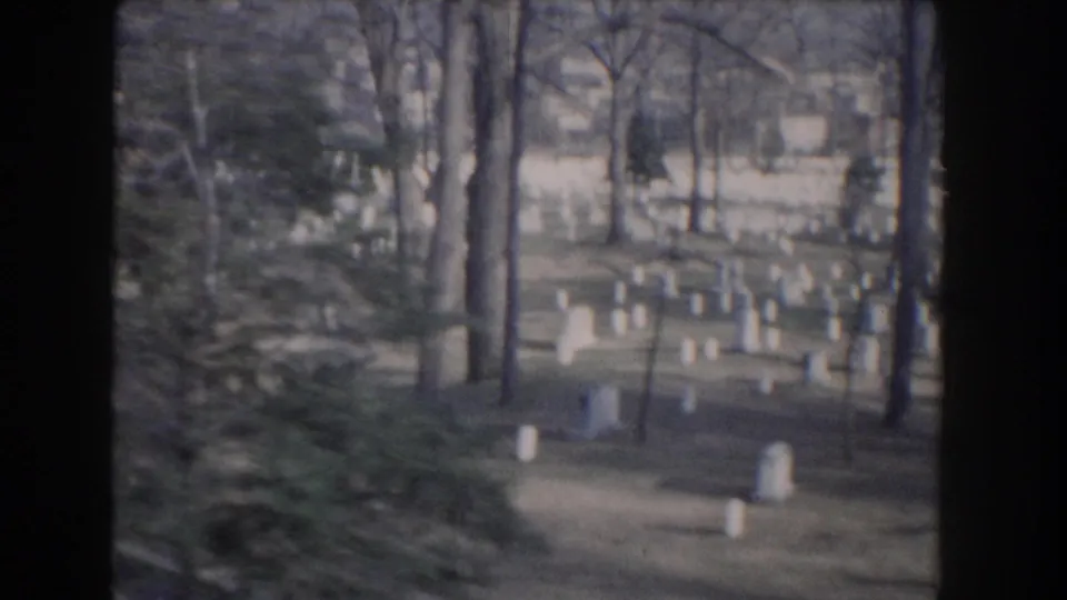 1960 Washington, DC home-movie view of white cemetery headstones scattered among bare trees and lawn.