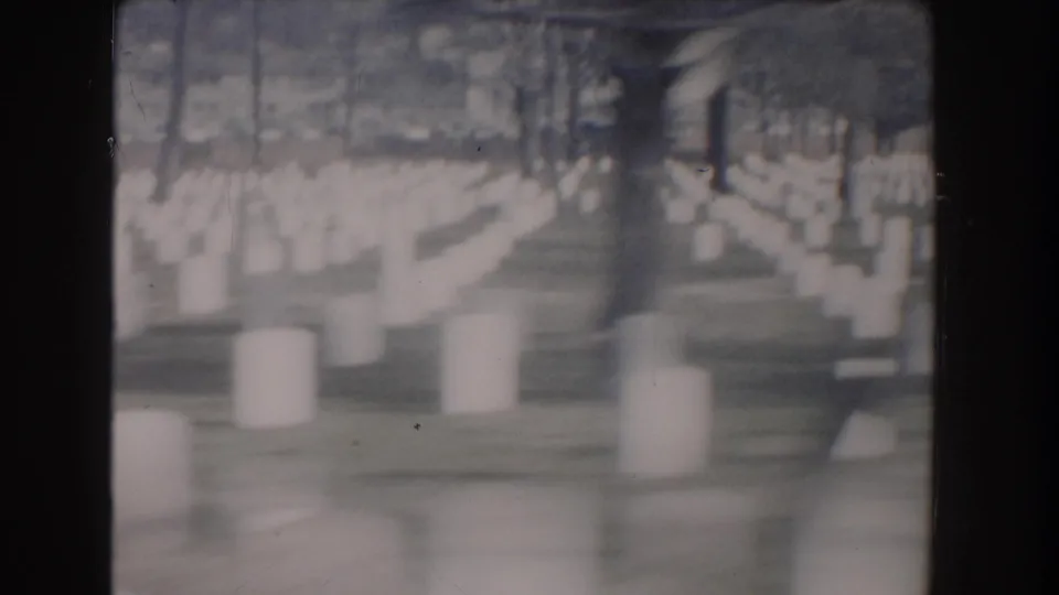 Rows of white military cemetery markers stretch across the lawn in soft 8mm focus.