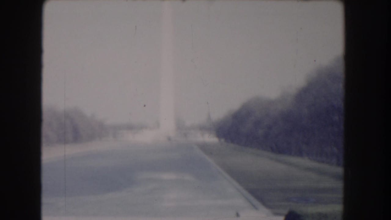 Distant Washington Monument viewed across the National Mall with trees and paths.