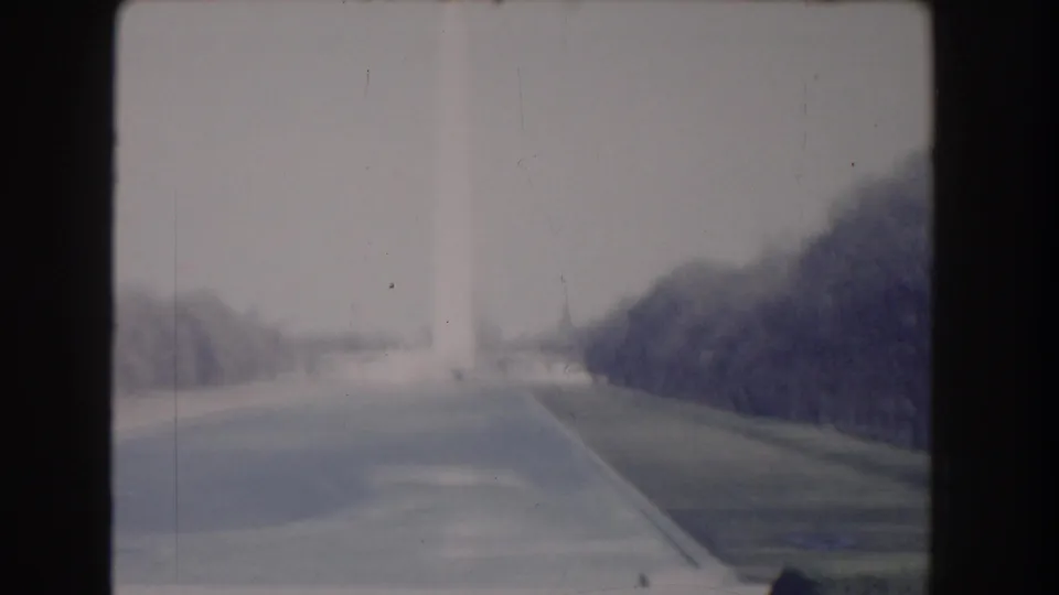 1960 8mm view of the Washington Monument rising through haze beyond tree-lined Mall paths in Washington, DC.