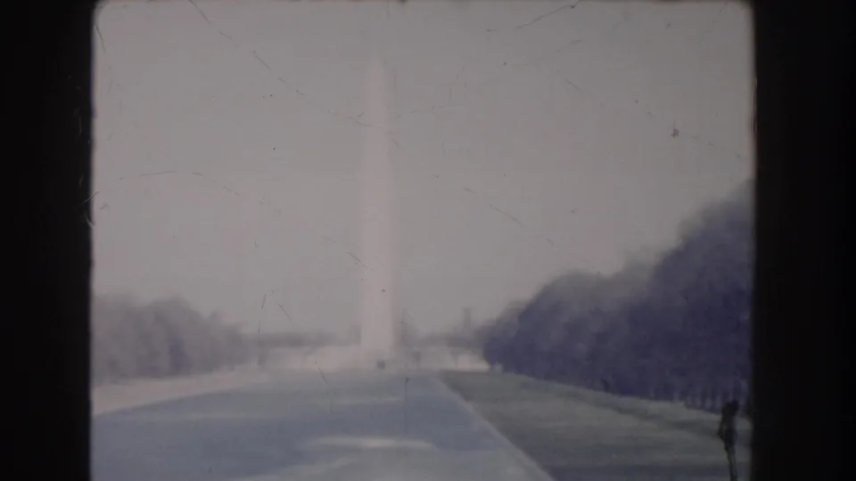 Distant 1960 home-movie frame of the Washington Monument and National Mall paths under a pale sky.