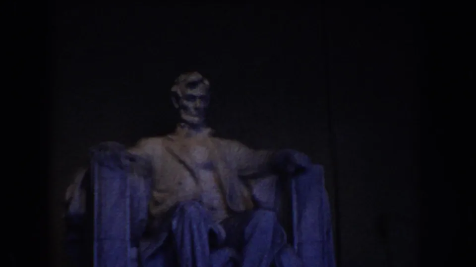 1960 Washington DC home-movie frame showing the seated Abraham Lincoln statue inside the Lincoln Memorial under dim blue lighting.