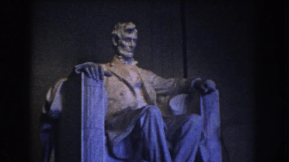 1960 Washington, DC home-movie frame showing the seated Lincoln statue inside the Lincoln Memorial with dark interior walls and blue-toned exposure.