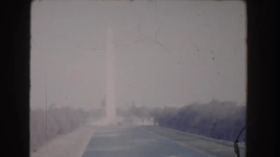 1960 Washington, DC frame showing the Washington Monument faintly in the distance beyond the Mall lawn, with visible film wear and muted color.