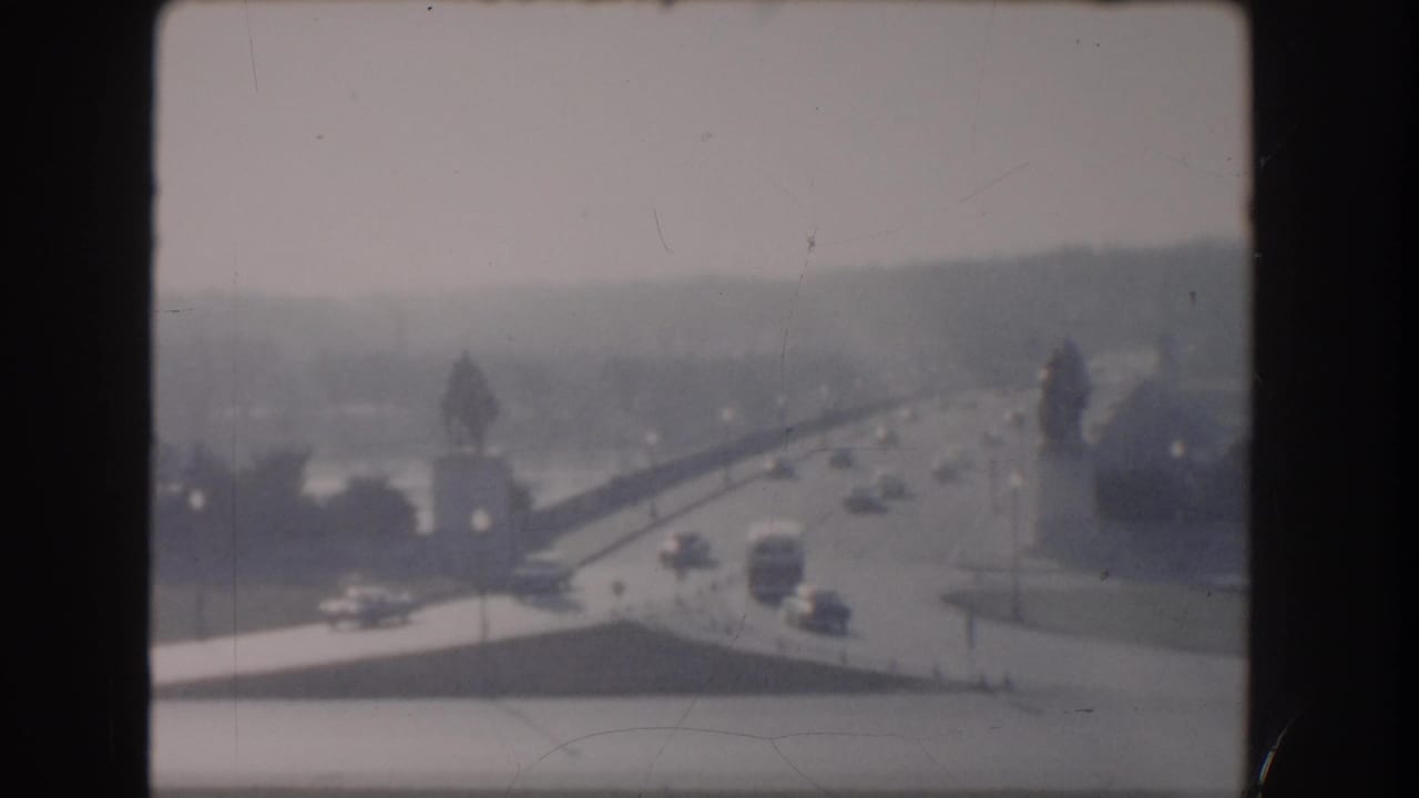 Elevated hazy view of a bridge approach with cars and buses moving through a broad roadway.