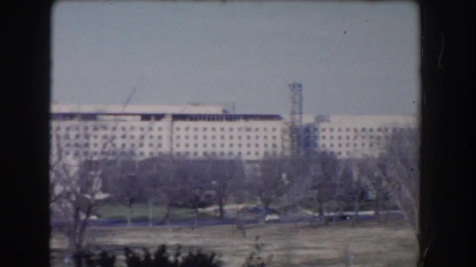 Washington, DC home-movie frame showing a large institutional building in the distance, with bare trees and open park-like ground in front.