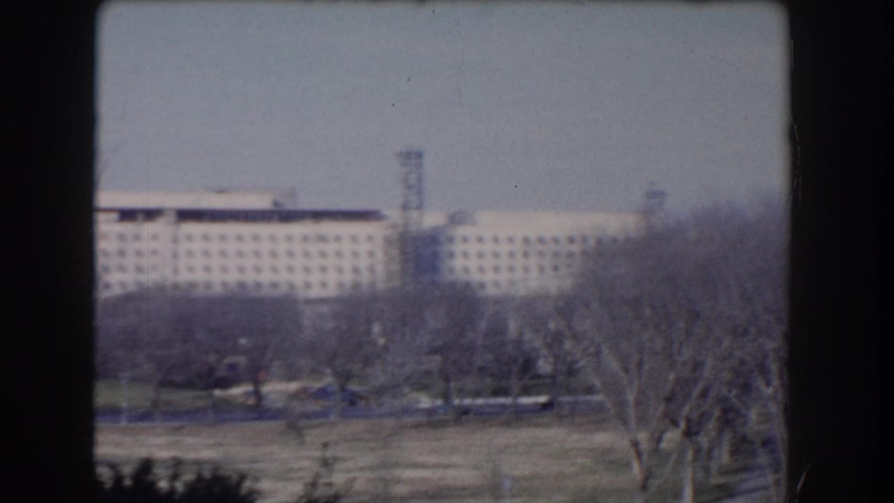 Distant large government building seen beyond leafless trees and open lawn.