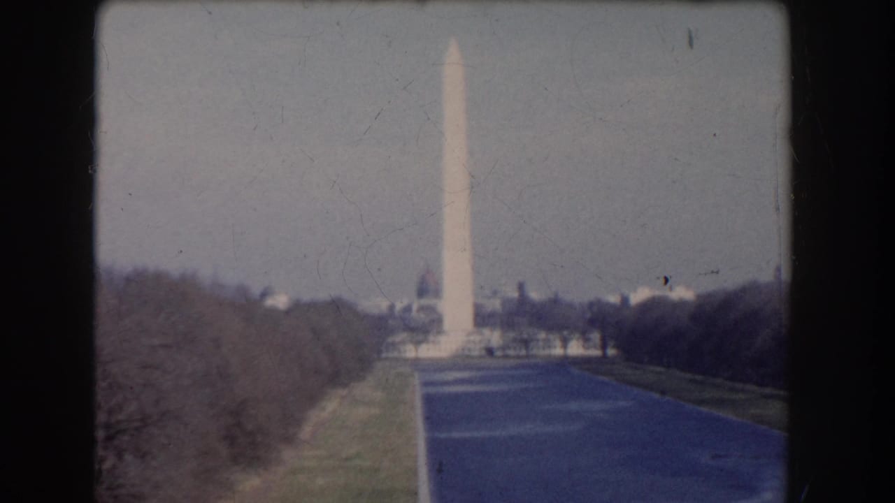 Distant Washington Monument seen across tree-lined grounds from an elevated home-movie viewpoint.