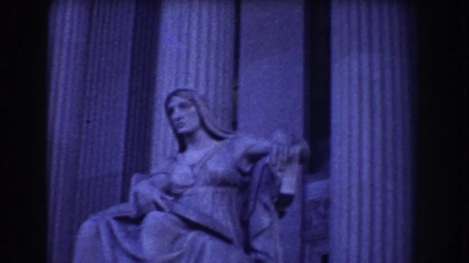 Close 8mm view of a seated classical statue and fluted columns, likely within a Washington, DC memorial setting.