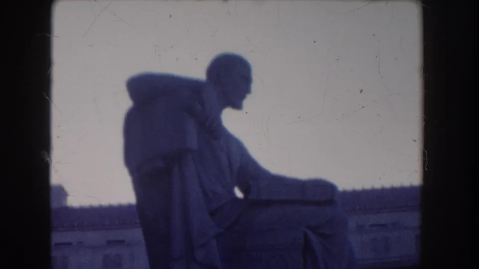 Final 1960 Washington, DC frame showing the seated robed statue from the side, with pale sky, roofline, and dark gate-like borders.