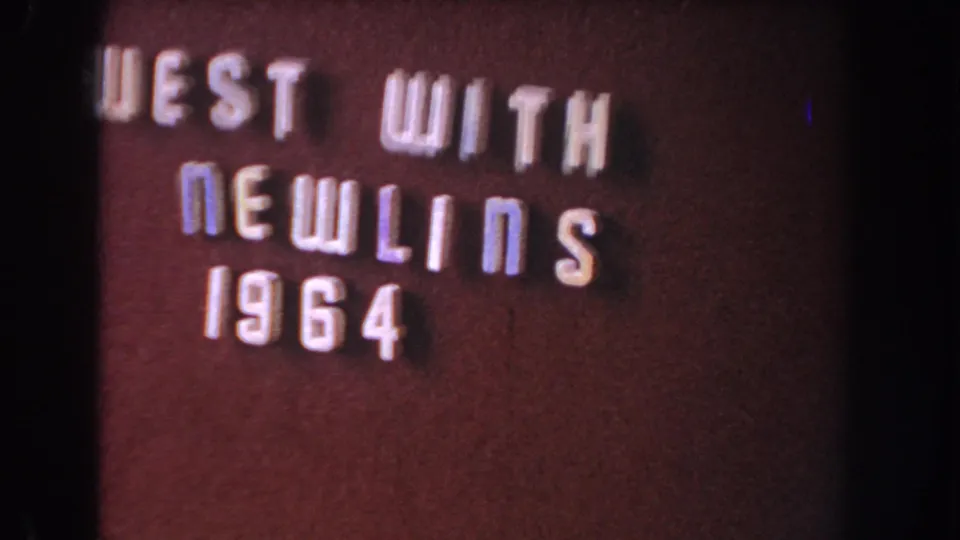The title card remains visible, reading "WEST WITH NEWLINS 1964," with a dark field, black gate edge and archival color shift.