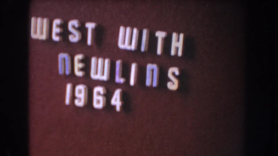 Close 8mm view of the dark title card, where the raised letters "WEST WITH NEWLINS 1964" fill the left side of the frame.