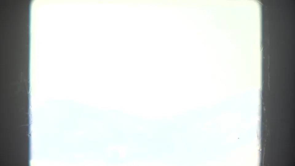 Overexposed 8mm landscape view showing pale sky, hazy distant mountains and a dark vertical frame or window edge at left.
