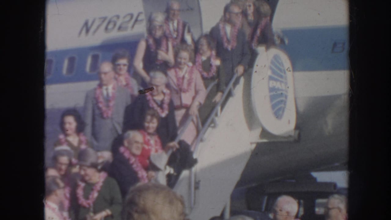 A crowded stairway beside a Pan Am aircraft shows travelers in leis moving toward the ground.