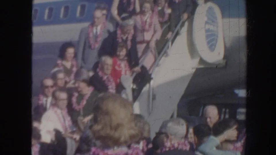 The 1961 Hawaii arrival continues with lei-wearing passengers on the aircraft stairs and a crowd of greeters and travelers filling the lower frame.