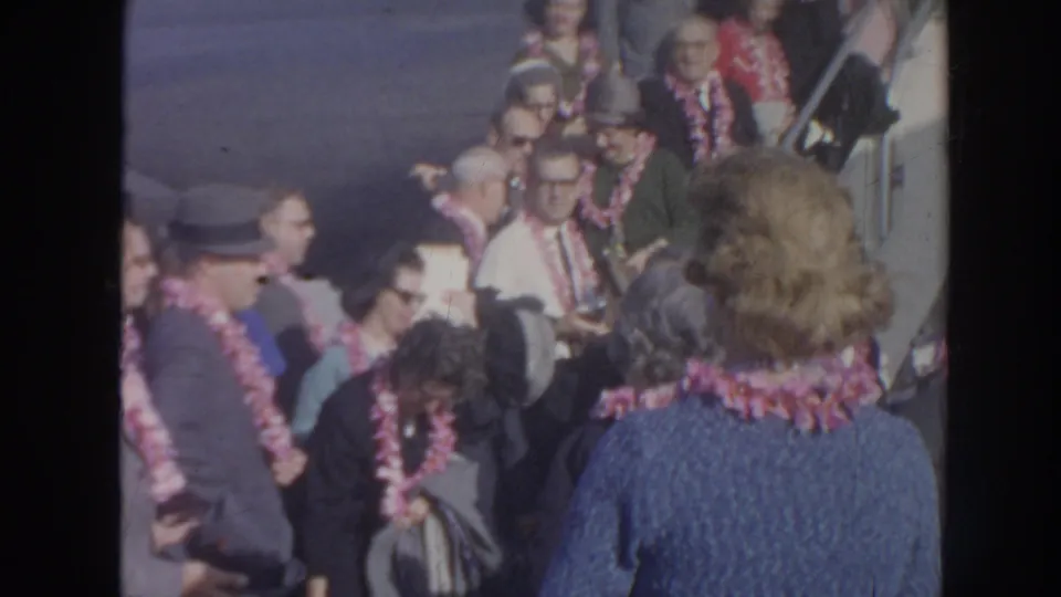 At the end of the 1961 Hawaii airport clip, passengers and greeters wearing leis cluster near the aircraft stairs after disembarking.