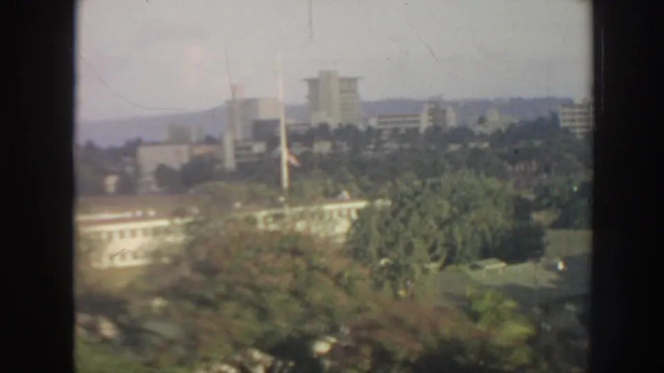1961 Hawaii cityscape showing low white buildings, taller blocks, palms, and distant hills through soft 8mm focus.