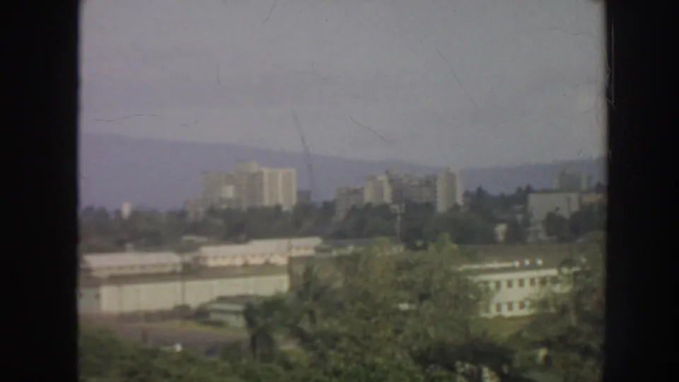 1961 Hawaii elevated view over trees and low structures toward distant towers and hazy hills.