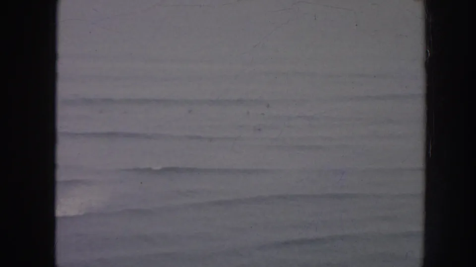 Muted 1961 Hawaii home-movie frame showing distant surf and layered waves under soft exposure.
