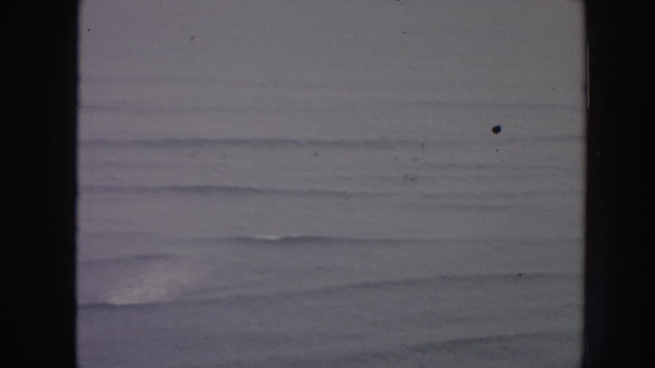 1961 Hawaii 8mm frame showing distant ocean swells and white surf lines through soft focus and visible film gate edges.