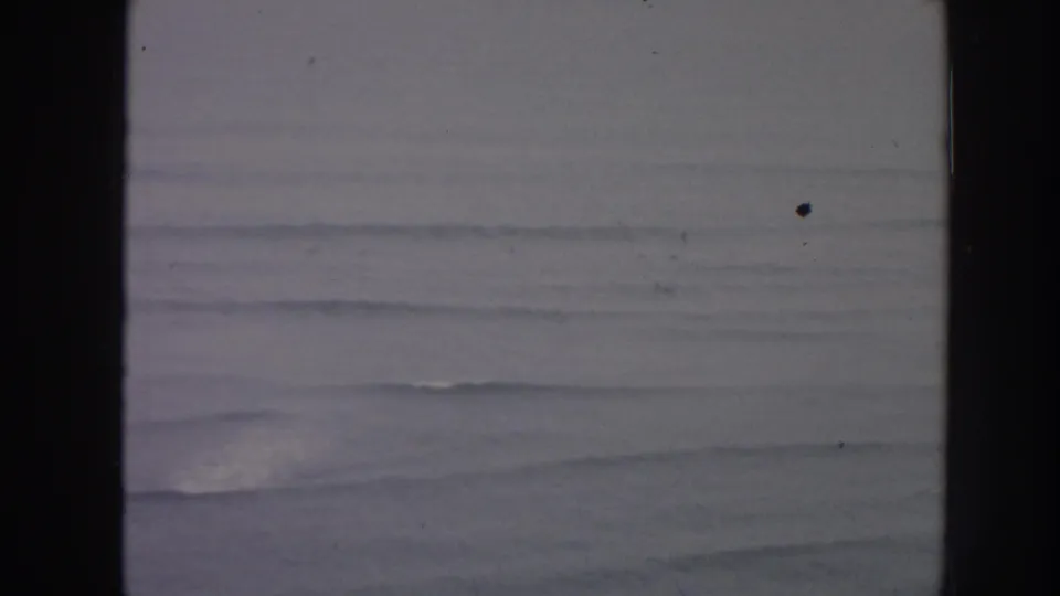 1961 Hawaii 8mm frame showing distant ocean swells and white surf lines through soft focus and visible film gate edges.