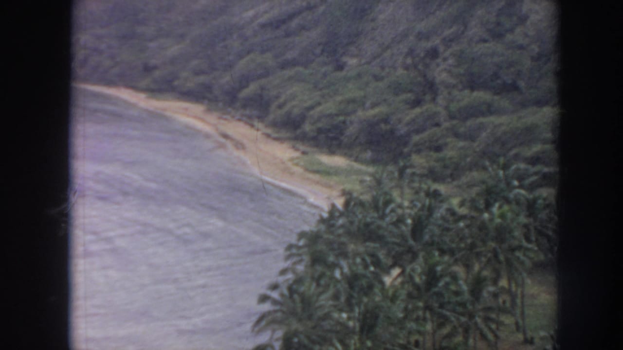 1961 Hawaii home-movie view over a curved beach, calm water, palms, and lush hills near Hanauma Bay.