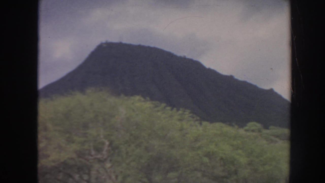 Dark mountain ridge above green vegetation seen through film-frame edges.