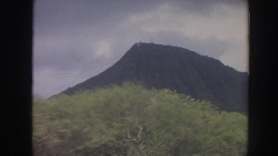 1961 Hawaii home-movie view of a mountain ridge behind dense green vegetation on an overcast day.
