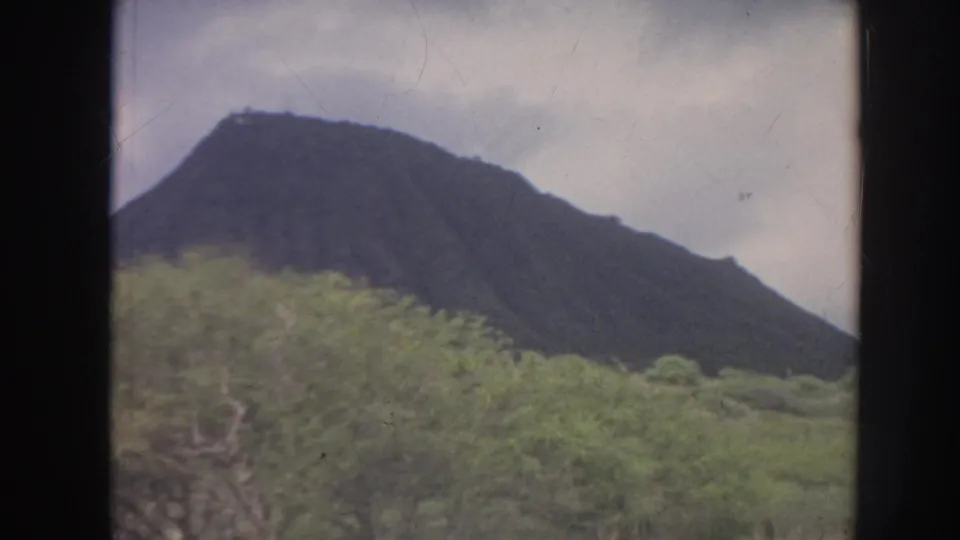 1961 Hawaii 8mm view of a mountain ridge above lush vegetation, with dark gate edges and muted color.