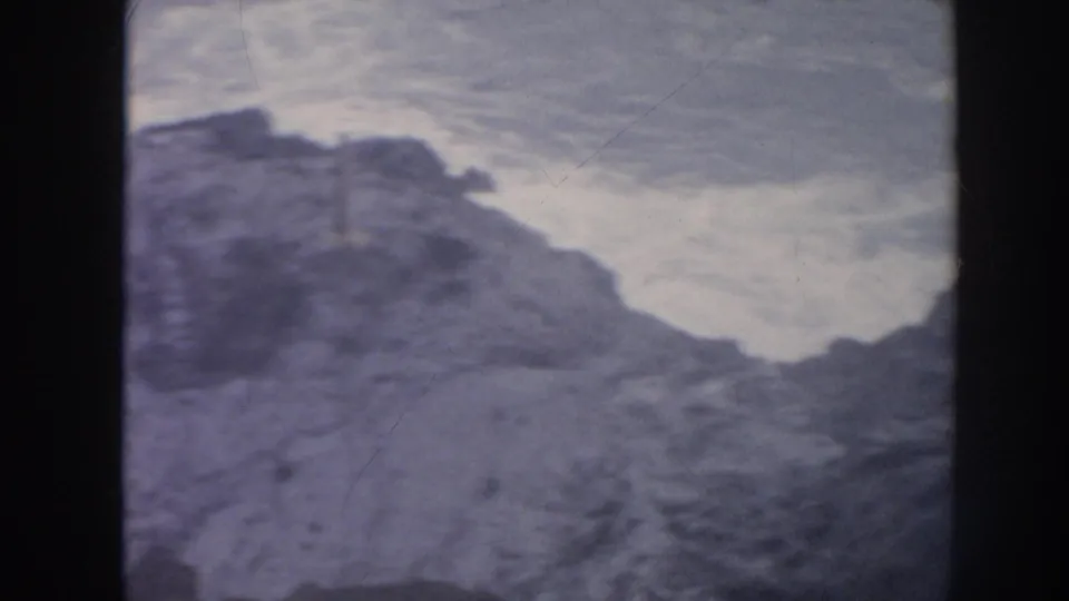 1961 Hawaii 8mm frame of dark coastal rocks beside white surf and turbulent blue-gray ocean water.