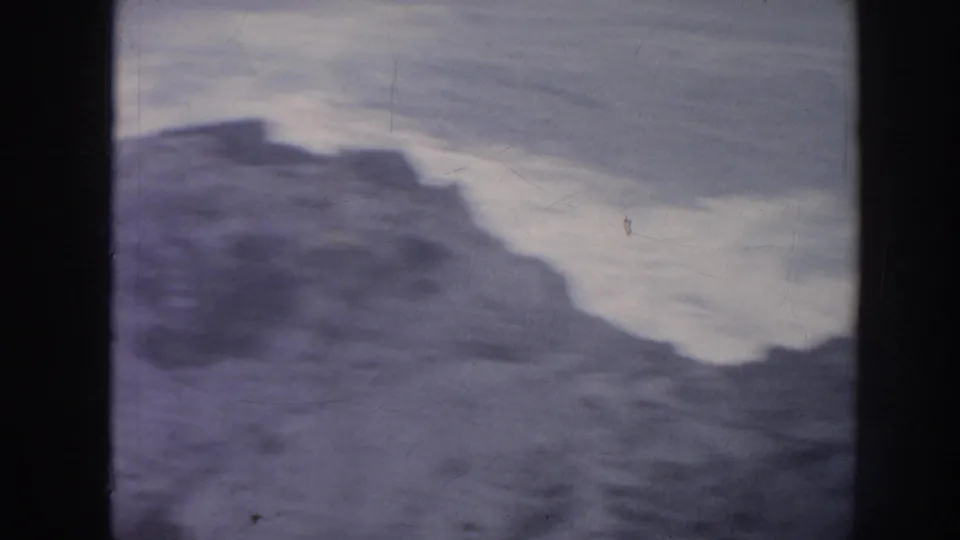 1961 Hawaii 8mm view of foamy ocean water moving around dark shoreline rocks, with visible film texture.