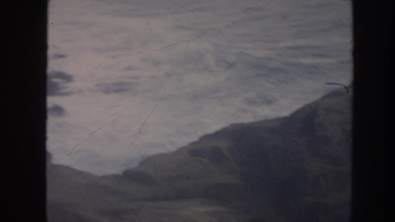 1961 Hawaii coastal view with rough water, distant headland, and prominent film gate shadow dividing the frame.