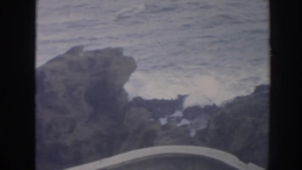 1961 Hawaii 8mm view of foamy surf between jagged rocks, with a partial curved foreground edge visible.